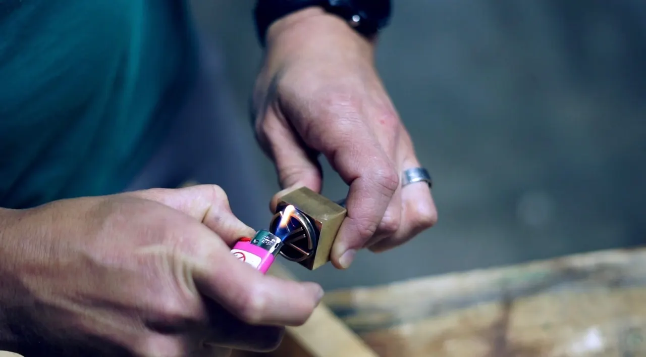 Hands heating the brass KT Leather branding stamp with a lighter at the workbench
